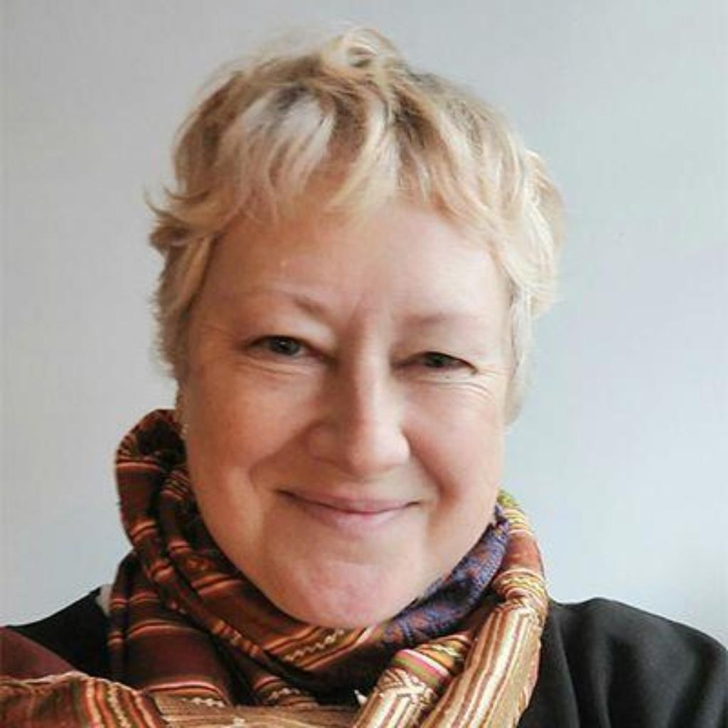 Porträt von Andrea Mbarushimana mit kurzen, hellblonden Haaren und einem bunt gemusterten Schal vor hellem Hintergrund